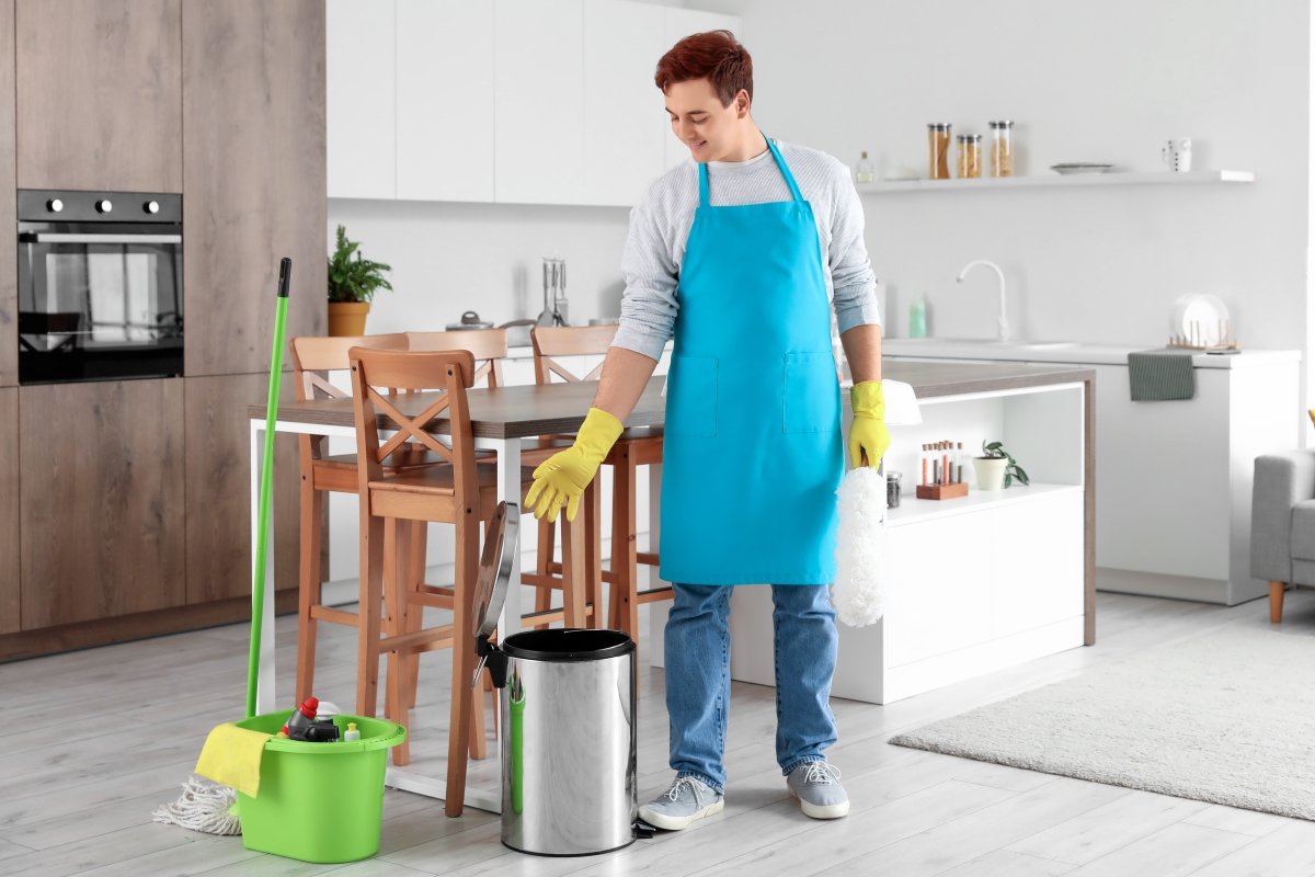A young man with cleaning supplies is looking to clean the indoor trash can. 