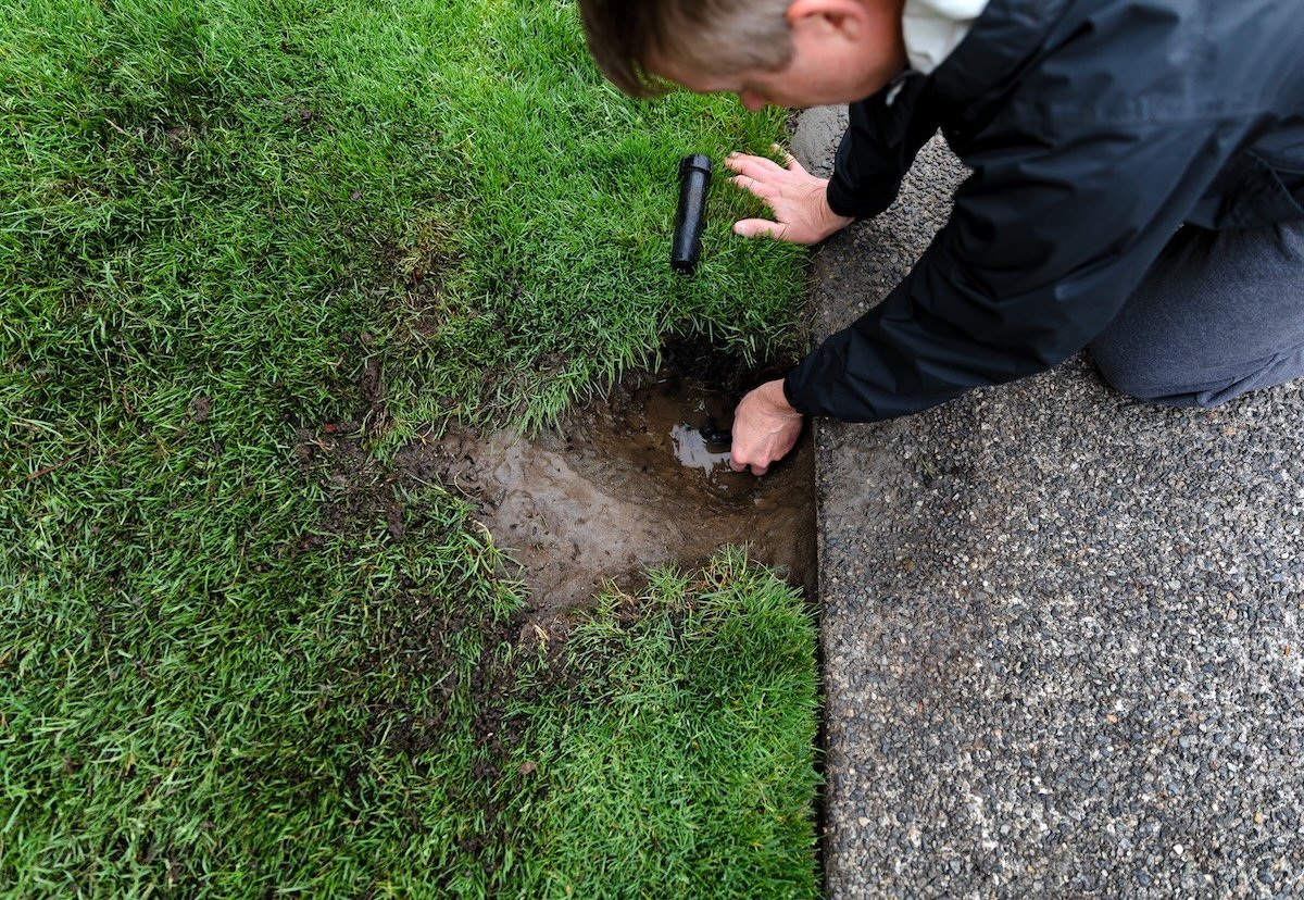 A DIYer repairing a broken sprinkler head on an irrigation system.
