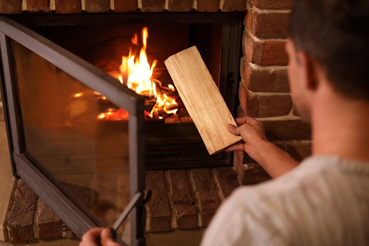 A person adding a log of firewood to a home wood-burning fireplace.