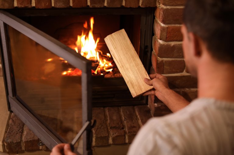 A person adding a log of firewood to a home wood-burning fireplace.