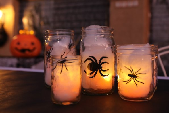 Handmade decorative Halloween mason jars filled with lights, spiders, and spider webs.
