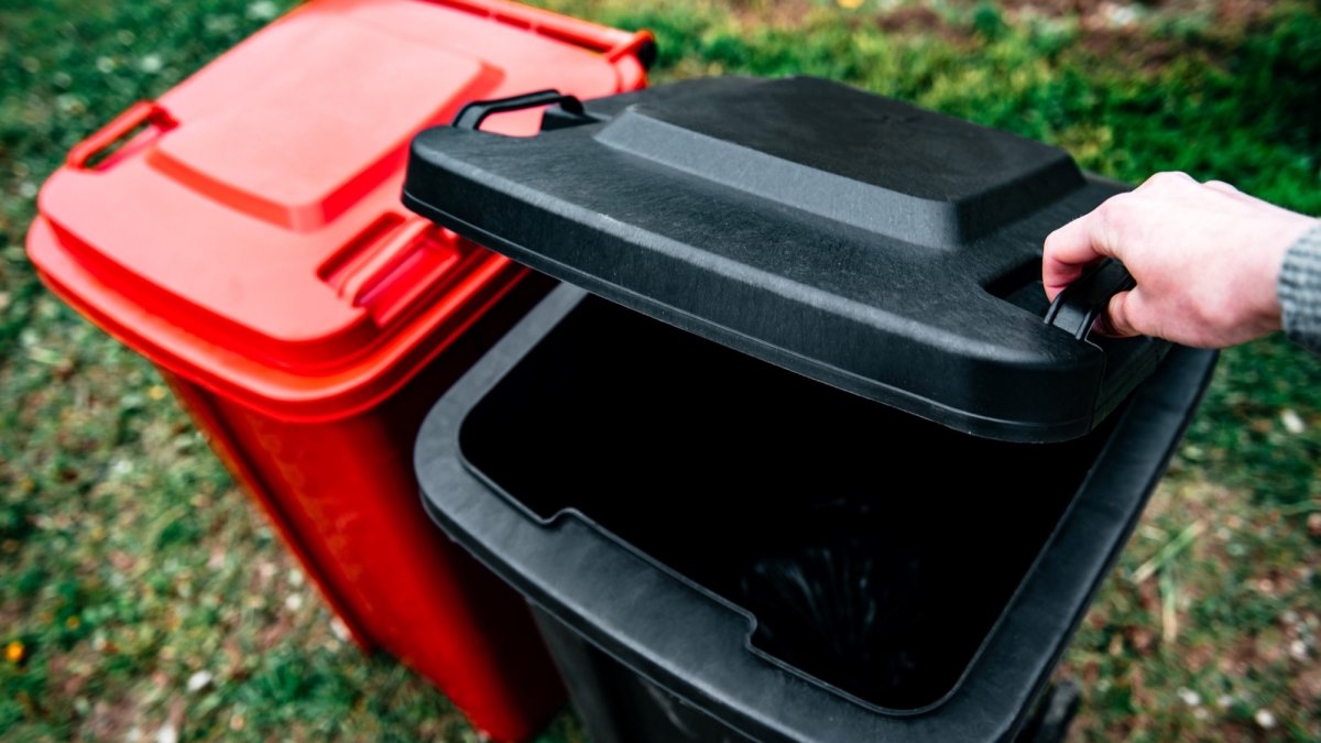 A hand is opening the lid of the outdoor trash can.