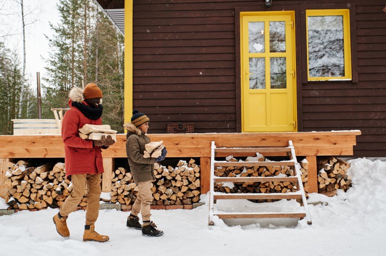 A father and son carry firewood to organize near a wintery cabin.