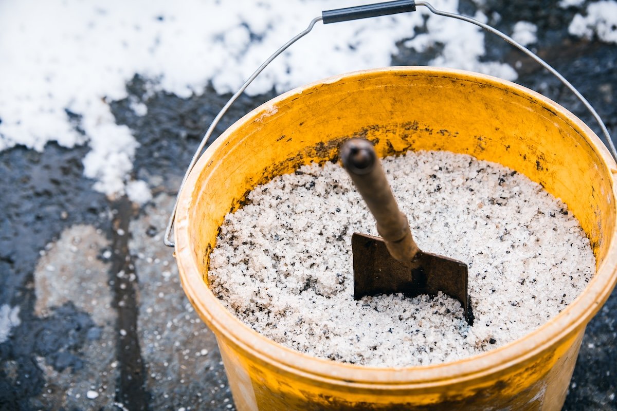 A yellow bucket with ice melt sand and a scoop.