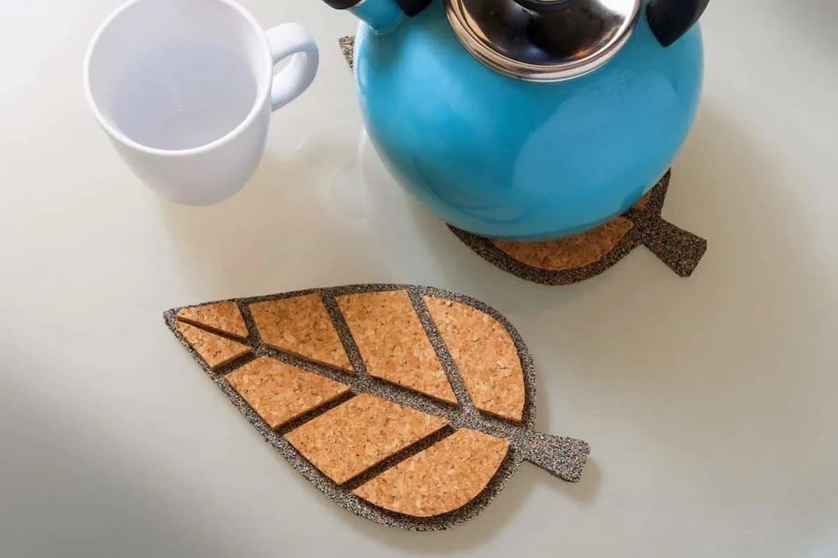 A cork coaster is shaped as a leaf next to a kettle and cup.