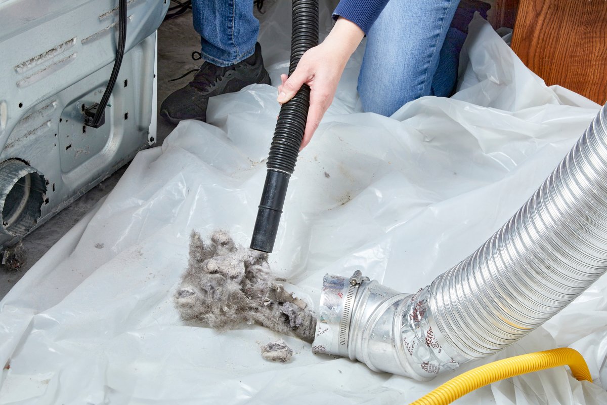 Woman wearing jeans crouches to vacuum up dryer lint using a vacuum attachment.