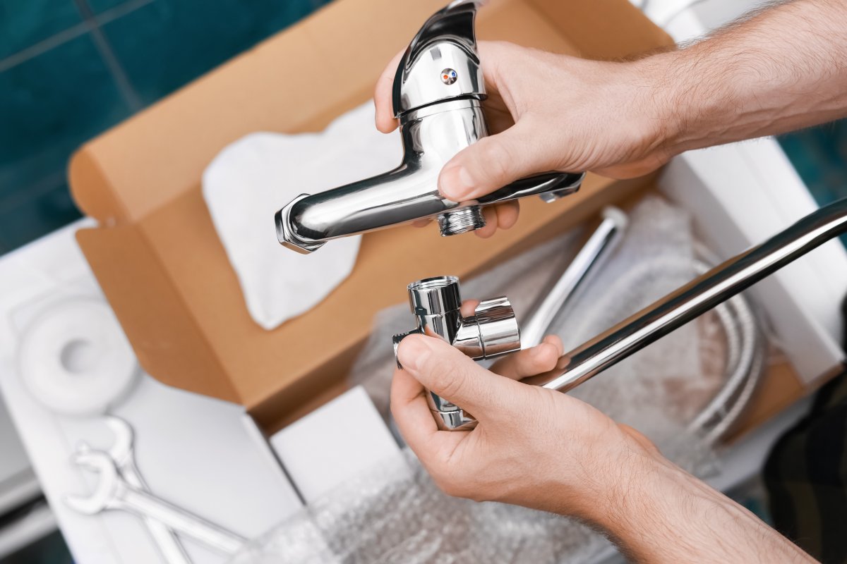 A man holds pieces of a new bathroom faucet in his hands, the open box visible underneath.