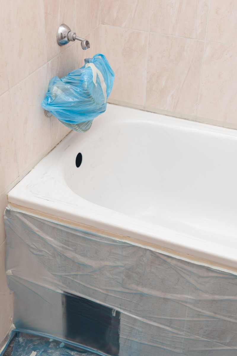 Bathtub prepared for reglazing, faucet wrapped and area covered with plastic film.