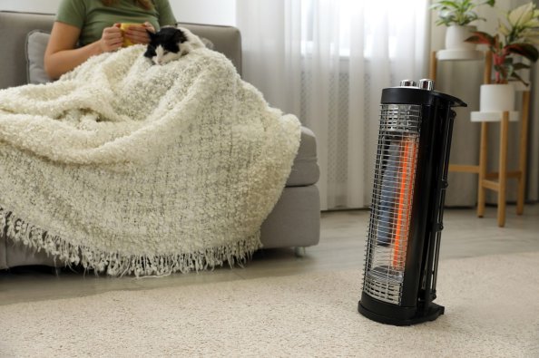 Woman sitting on a couch with cat and blanket warming up with a space heater