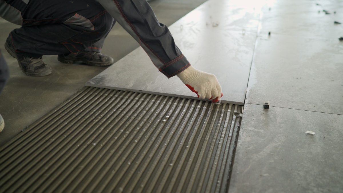 Man installing a large ceramic tile on the floor.