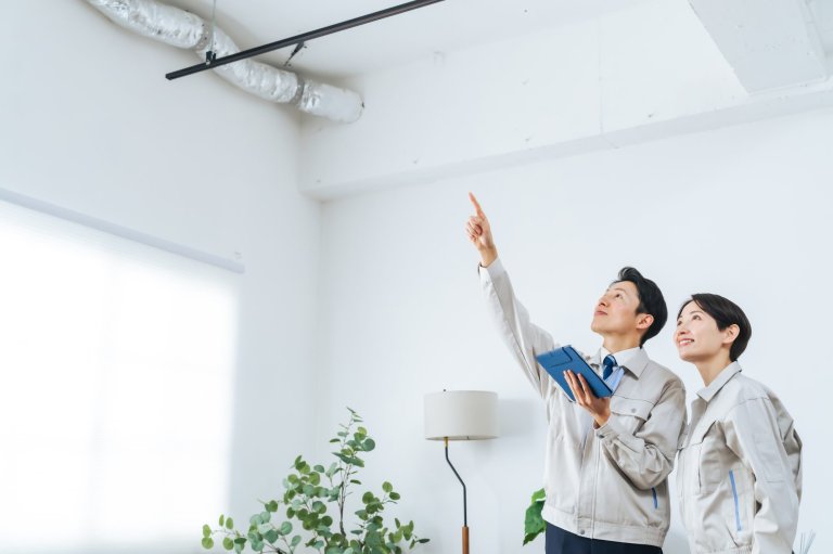 Man and woman looking up and pointing at exposed pipes and ducts in a room.