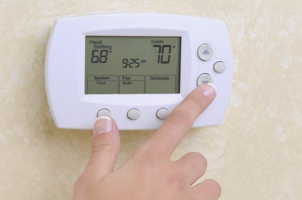 Closeup of a woman's hand setting the room temperature on a programmable thermostat.