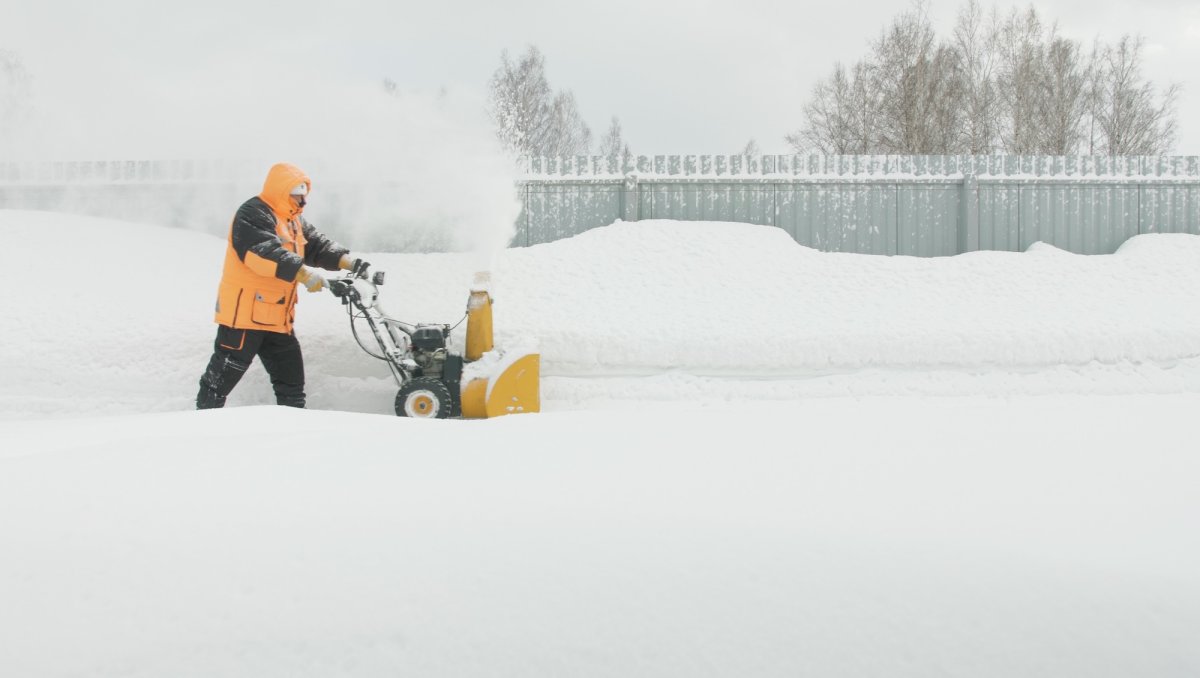 A man wearing an orange parka snow blows during a blizzard.