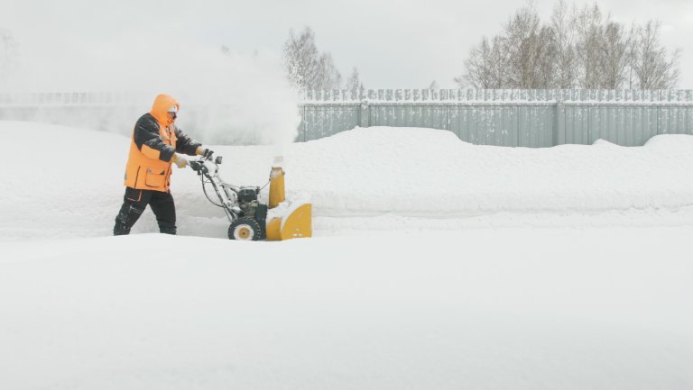 A man wearing an orange parka snow blows during a blizzard.