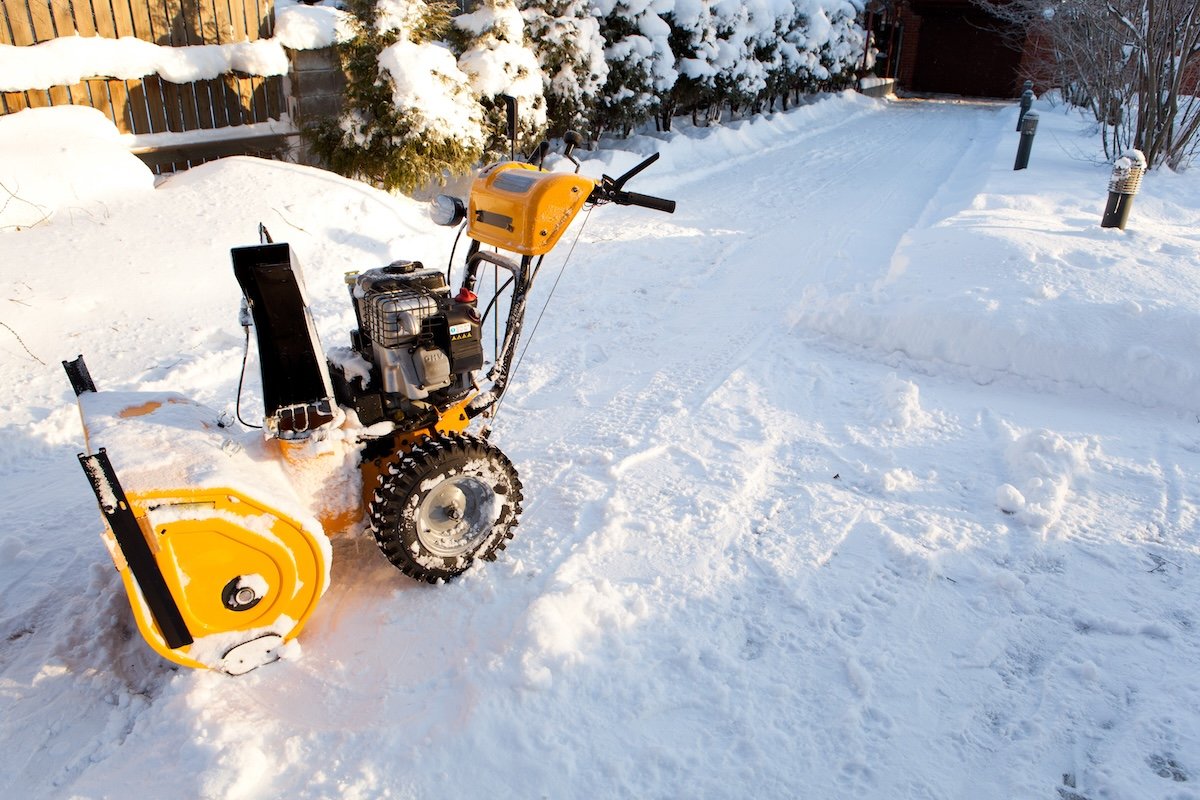 A standing yellow snowblower on a sidewalk.