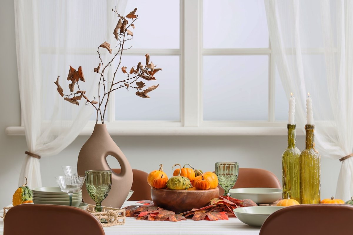 Thanksgiving dinner table setting with branches in a vase in a cozy dining room interior.