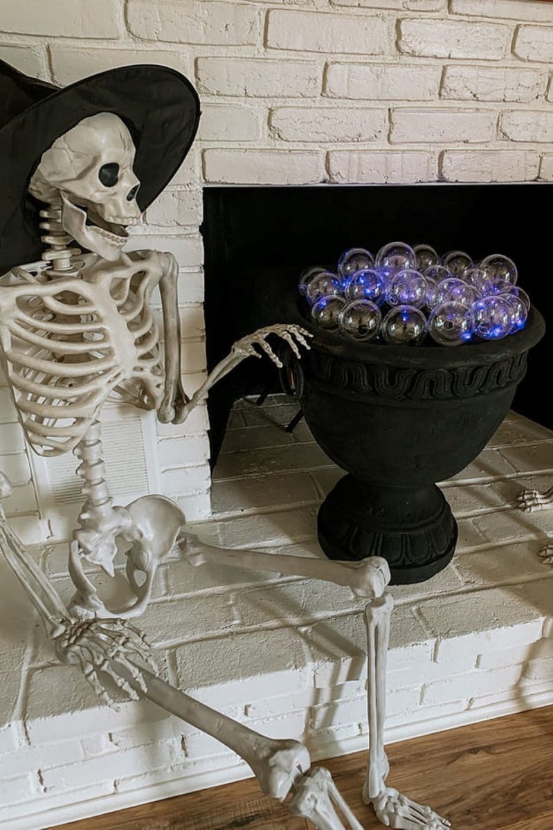 A skeleton with a witch's hat is placed next to a DIY cauldron.
