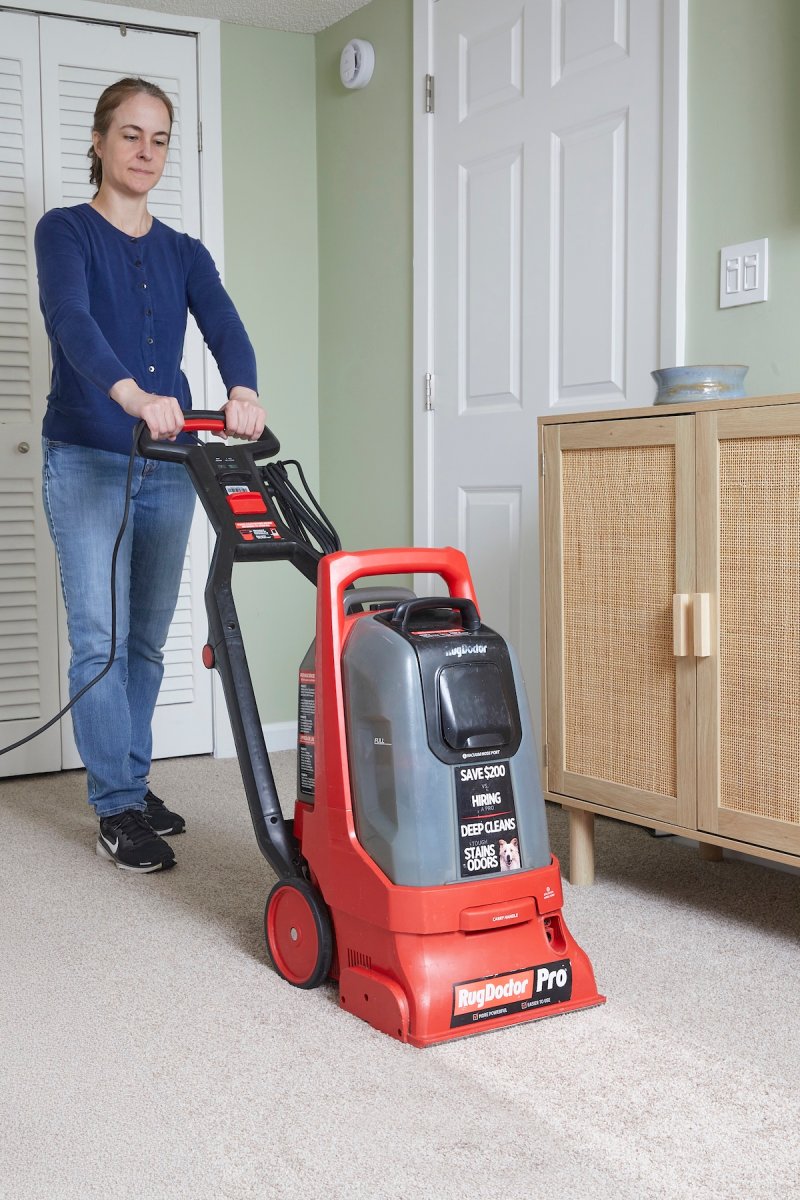 Woman pushing a red carpet cleaner on a light carpet.