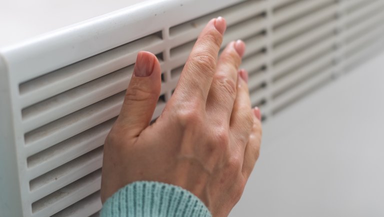 Close-up of a woman's hand and sleeve of sweater over a white vent and wall. all.